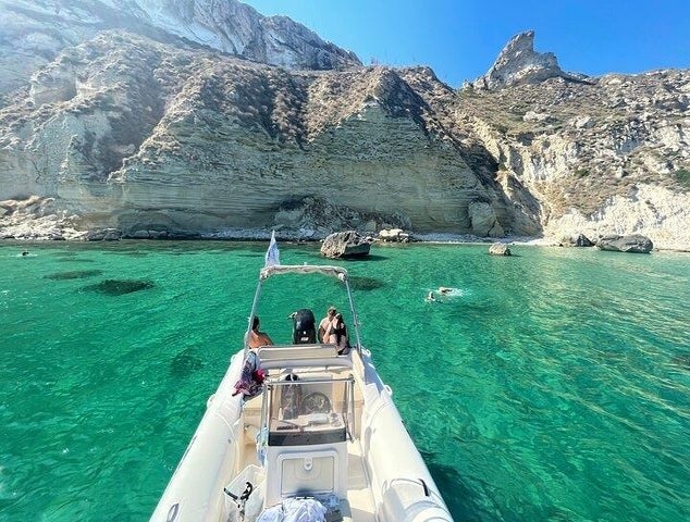 A small boat with people on board floats on clear turquoise water near the rocky cliffs of Devil-s Saddle in Cagliari..jpg