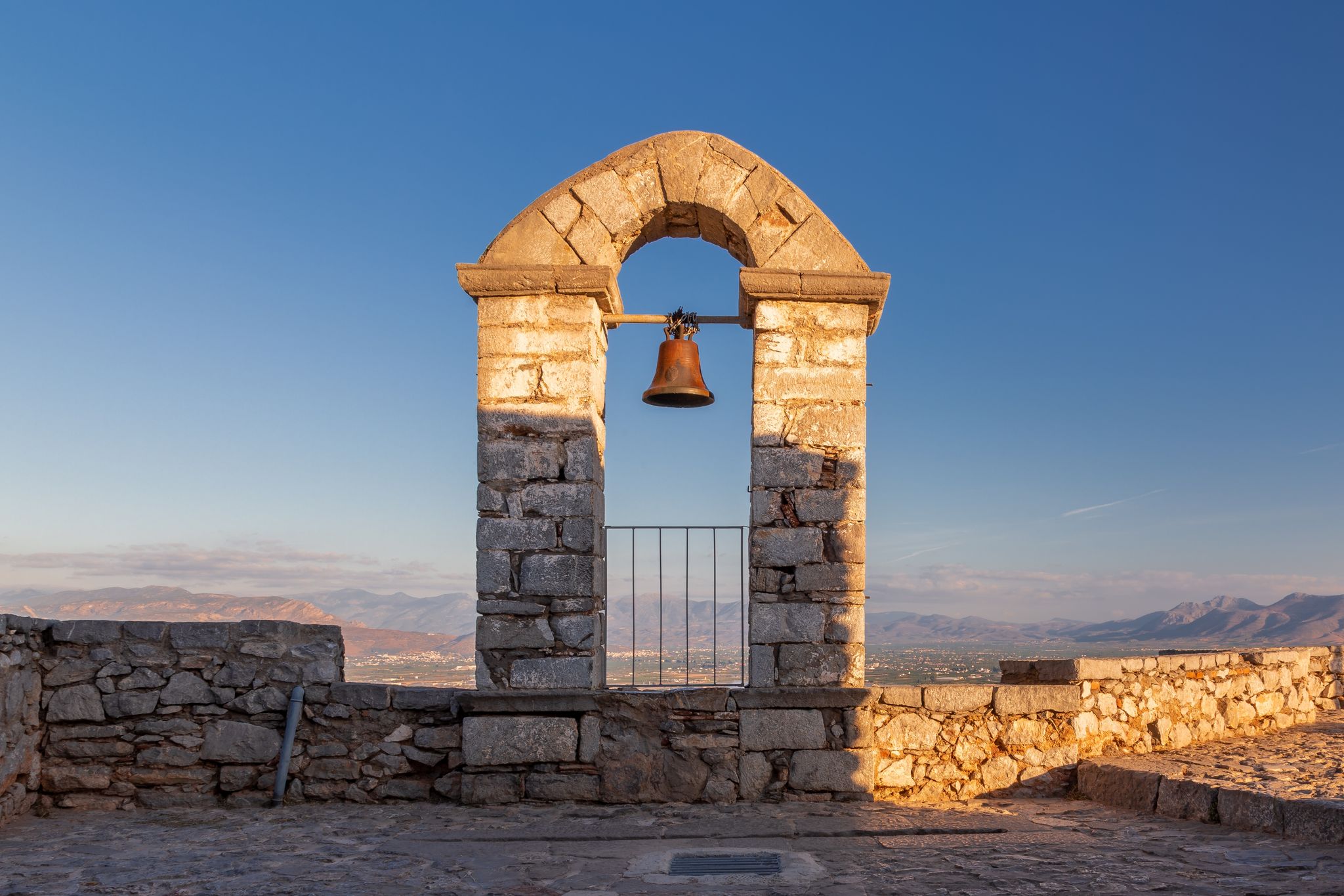 Photo of Bell tower in Palamidi fortress on a hill above vast valley surrounded by mountains, Nafplio, Greece.