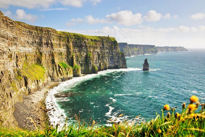 The Cliffs of Moher in Ireland rise above the Atlantic Ocean, with green slopes and a sea stack in the water..jpg