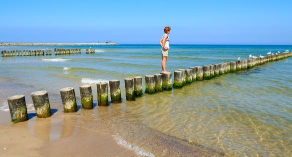 Young woman tourist standing on wooden breakwaters on beach in Ustka seaside town, Baltic Sea, Poland