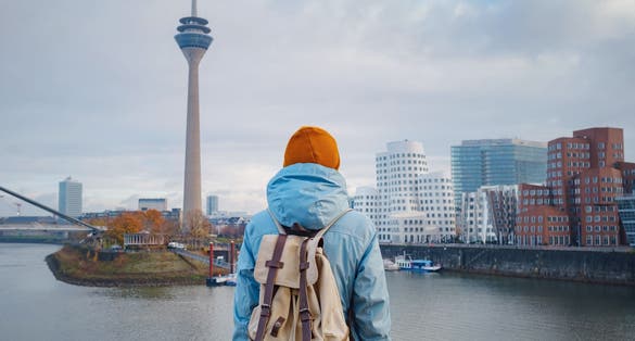 photo of view  of  autumn or winter travel to Dusseldorf, Germany. young Asian tourist or student in blue jacket and yellow hat ( symbol of Ukraine) walks through sights of European city. beautiful view in the Media Bay