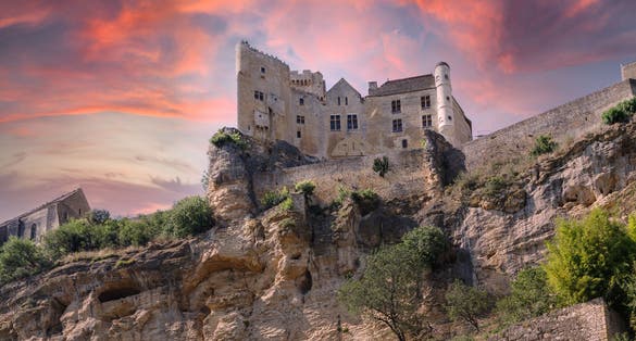 photo of Chateau de Beynac on the rock against dramatic sunset sky in Village of Beynac-et-Cazenac, France.