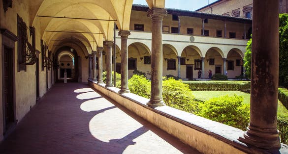 photo of view of Courtyard Basilica di San Lorenzo (Basilica of St Lawrence) with arches, columns and garden on sunny day, Florence, Italy.