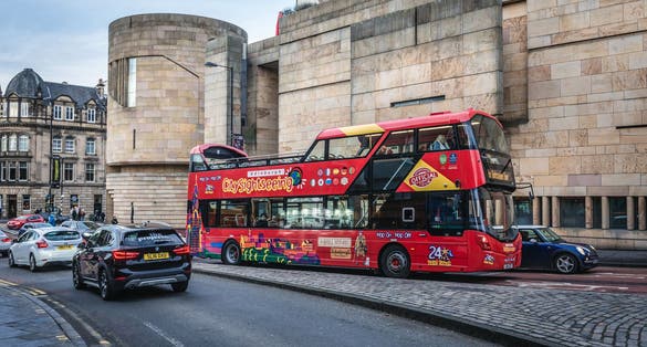  City Sightseeing Hop-On Hop-Off bus in front of National Museum of Scotland in Edinburgh city.