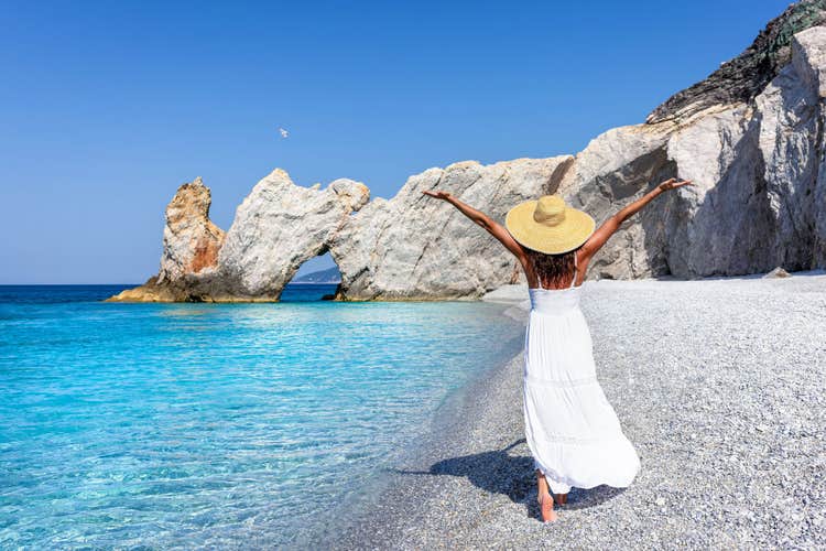 Photo of tourist woman in a white summer dress enjoys the beautiful beach of Lalaria, Skiathos island, Greece.