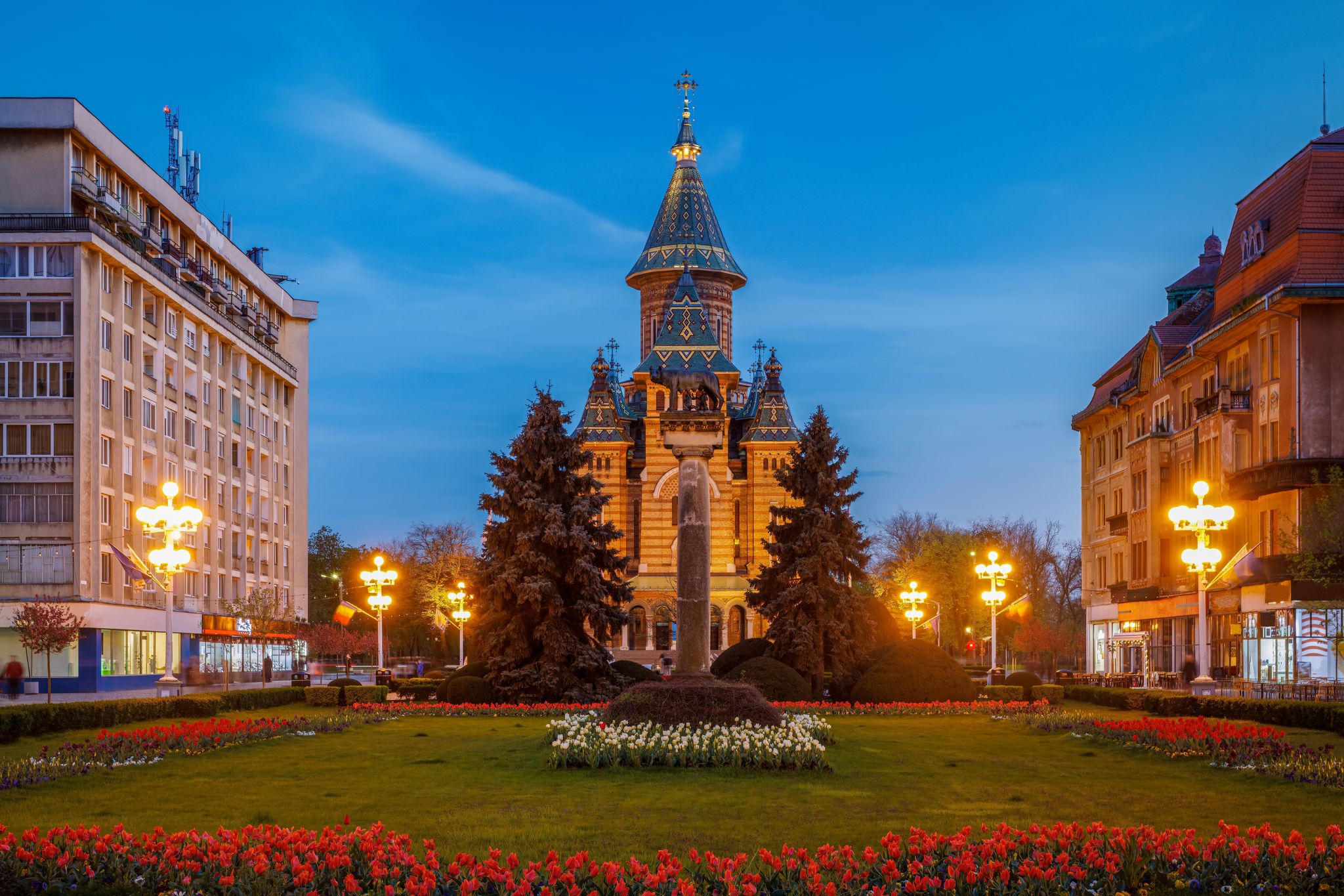 Photo of Victory square at night, piata victoriei Timisoara is a long square with green park surrounded by national opera on one side and the metropolitan cathedral on the other.