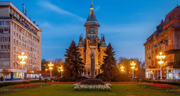 Photo of Victory square at night, piata victoriei Timisoara is a long square with green park surrounded by national opera on one side and the metropolitan cathedral on the other.
