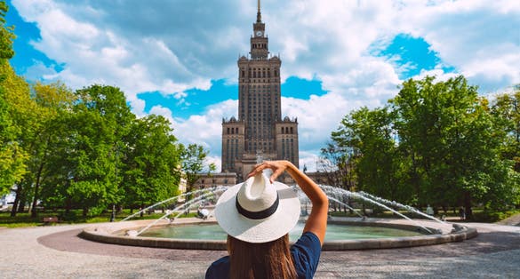 Photo of tourist woman in white sun hat walking in the park near Palace of Culture and Science in Warsaw, Poland.
