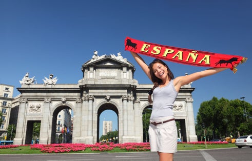 photo of tourist holding Espana banner in front of Puerta de Alaca on Plaza de la Independencia in Madrid, Spain.