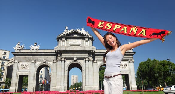 photo of tourist holding Espana banner in front of Puerta de Alaca on Plaza de la Independencia in Madrid, Spain.