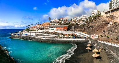 Atlantic ocean beach, playa de Santiago, waves crashing on coastline, people walking along embankment, relaxing. Bay. Puerto de Santiago, south of Tenerife, Canary islands, Spain.