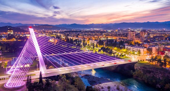 Photo of illuminated Millennium bridge in the city center, under colorful sunset sky, Podgorica, Montenegro, at night.