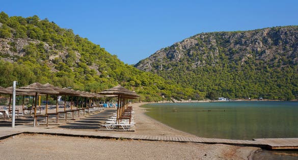 Photo of sunbeds with umbrellas on the famous beautiful lake Vouliagmeni with blue sky in Loutraki, Perachora, Greece.