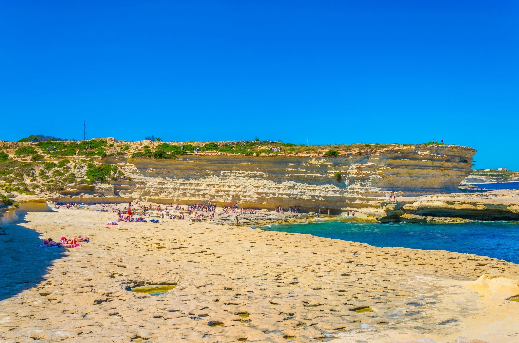 Photo of crystal clear turquoise water in blue lagoon of St. Peters pool  rocky beach at Malta.