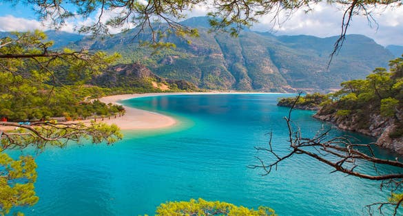 photo of amazing view of Blue Lagoon in Oludeniz, Turkey. Summer landscape with sea spit, green trees, azure water, sandy beach in bright sunny day. Top view of national park.