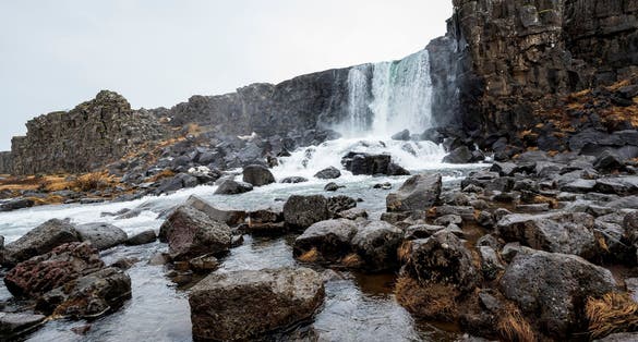 photo of the beautiful oxarárfoss waterfall flows from the river oxará over black basalt rocks into the almannagjá gorge, Þingvellir, Thingvellir national park, Golden circle route, Iceland.
