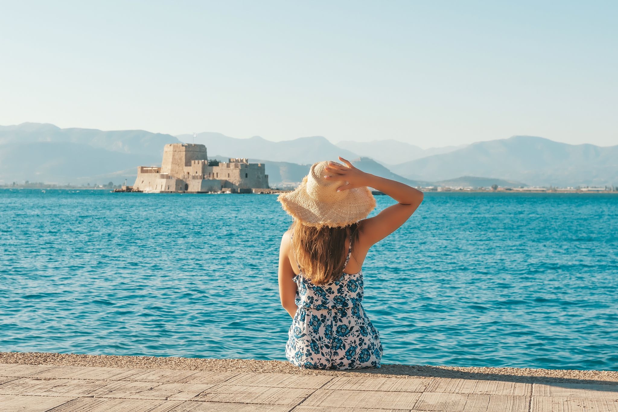 Photo of happy tourist sitting on the beach looking at the Bourtzi water castle is a small island with a fortress at the coast of Nafplio in Greece.