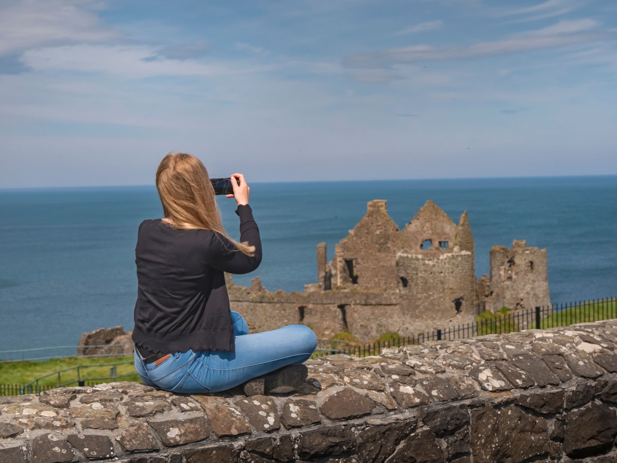 Young woman takes photos of Dunluce Castle in North Ireland.
