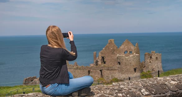 Young woman takes photos of Dunluce Castle in North Ireland.