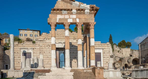 the ancient Roman ruins in Brescia, Italy, showcasing the weathered yet majestic columns of a temple. The detailed carvings and inscriptions on the stone structures reflect the grandeur
