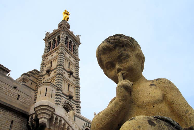 Close-up of a child statue with a finger to its lips in front of the bell tower of Notre-Dame de la Garde basilica in Marseille, France..jpg