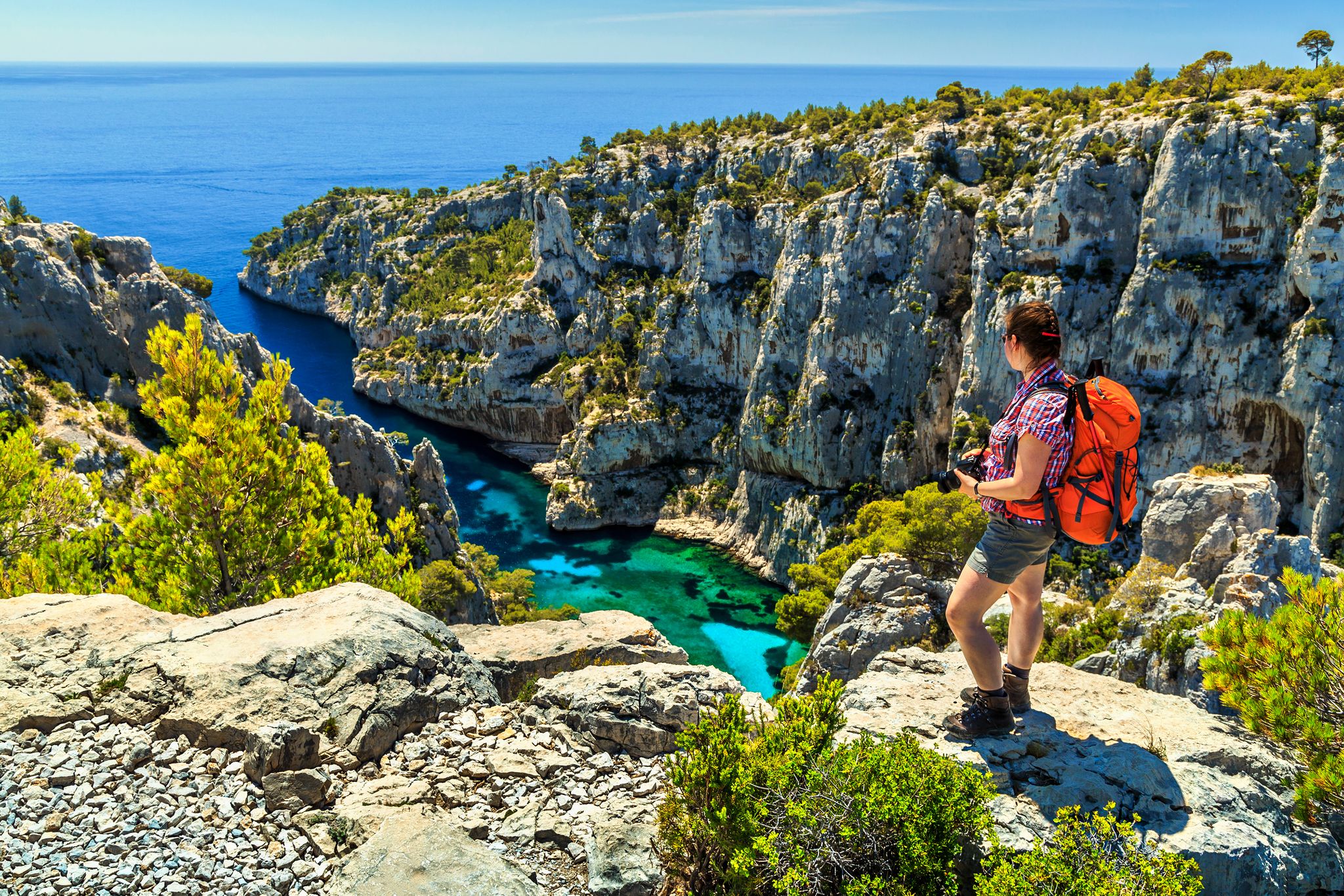 photo of young hiker woman with backpack and photo camera on the high cliffs at Calanques National Park near Cassis fishing village in Marseille, South France.