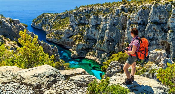 photo of young hiker woman with backpack and photo camera on the high cliffs at Calanques National Park near Cassis fishing village in Marseille, South France.