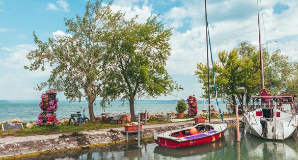 photo of view of View to entrance to Siofok harbor at Balaton lake, Hungary, with crystal clear water of emerald color, green coastline, puffy clouds on sky