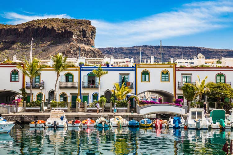 Traditional Colorful Buildings With Boats In Front And Mountain In The Background - Puerto de Mogan, Gran Canaria, Canary Islands, Spain