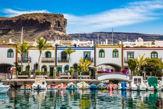 Traditional Colorful Buildings With Boats In Front And Mountain In The Background - Puerto de Mogan, Gran Canaria, Canary Islands, Spain