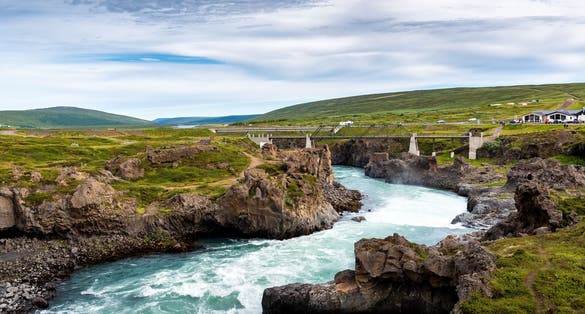 A river from Godafoss Falls, Akureyri, Iceland, surrounded by huge rocks and a concrete bridge