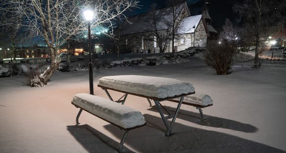 photo of night view of small park with bench covered with snow behind Åre Old Church in Åre, Sweden.