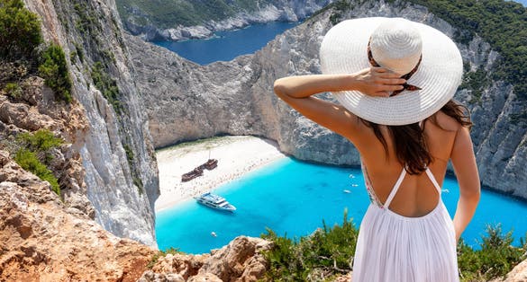 Photo of woman stands on a cliff and enjoys the breathtaking view to the famous shipwreck beach, Navagio, on Zakynthos island, Greece.