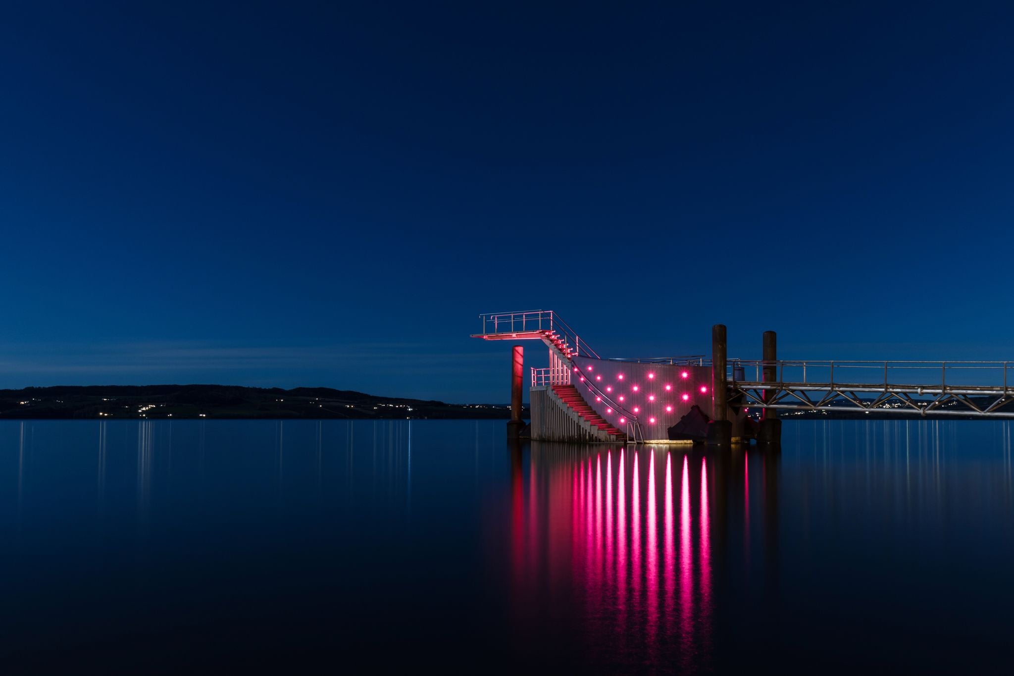 photo of view of Diving tower with pink lights on a pier in Hamar city, Norway. Beautiful blue night sky during autumn.