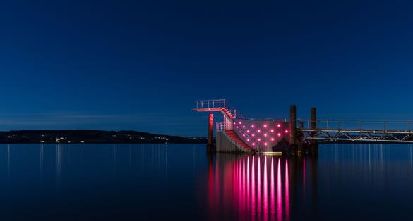 photo of view of Diving tower with pink lights on a pier in Hamar city, Norway. Beautiful blue night sky during autumn.