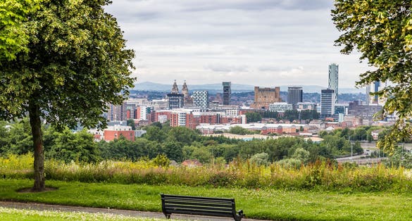 Photo of a bench seen lbetween trees overlooking the Liverpool skyline from Everton Park.