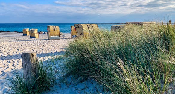 Photo of View of the sandy beach, traditional north german beach chairs and green beach grass on the island Fehmarn on Baltic sea.