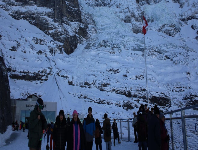 Visitors at the snowy Eiger Glacier viewpoint with a Swiss flag and Alpine mountain backdrop..jpg