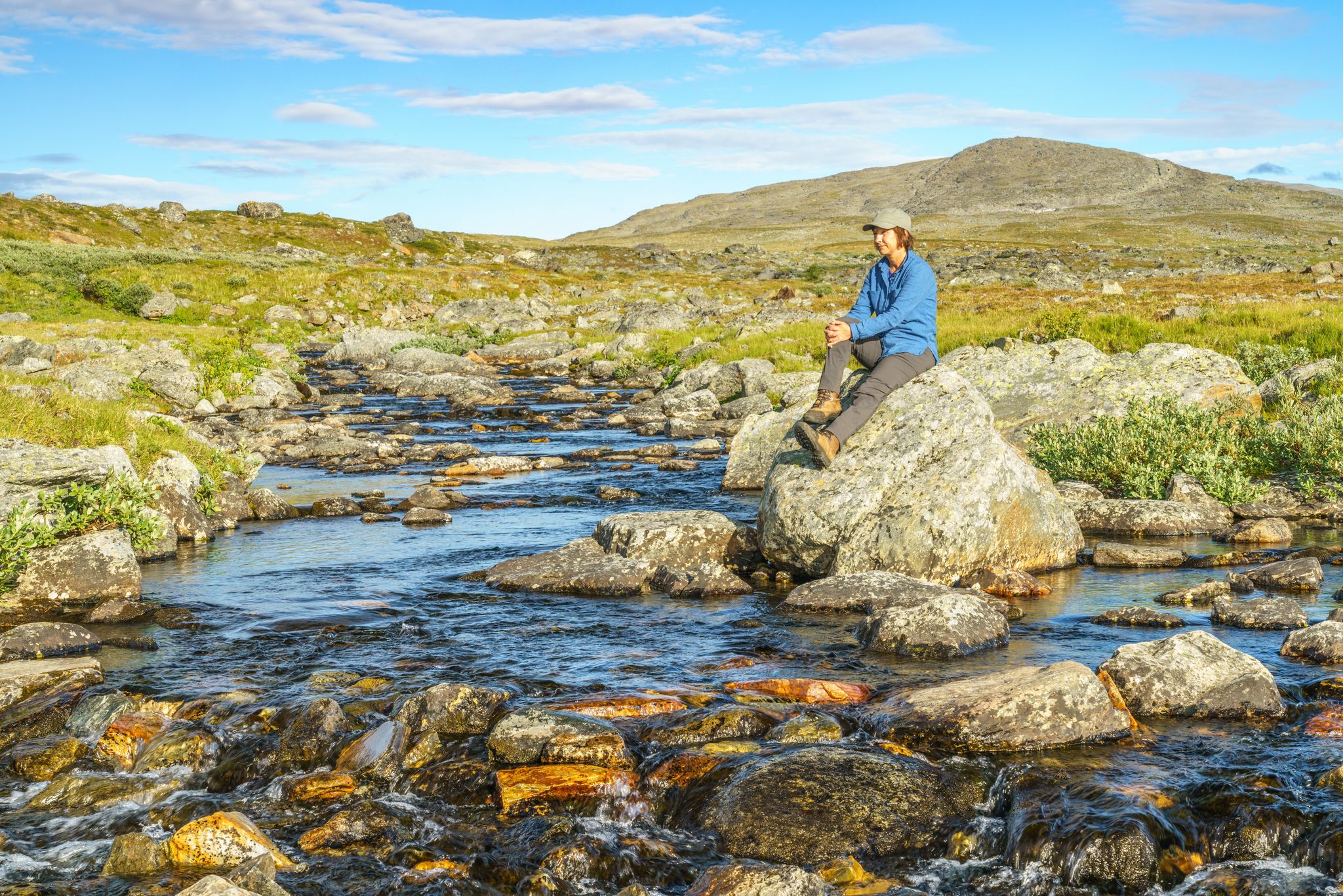 Woman sitting on a rock at a creek in mountain area along the kings trail, Gällivare county, Swedish Lapland, Sweden