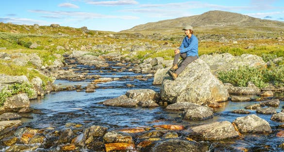 Woman sitting on a rock at a creek in mountain area along the kings trail, Gällivare county, Swedish Lapland, Sweden