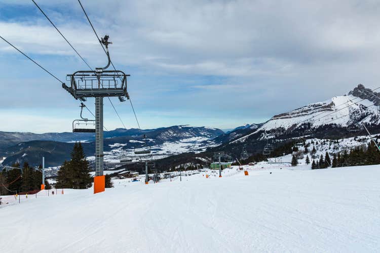 Empty chair lift at french Villard de Lans ski resort surrounded by snowy Vercors mountains.