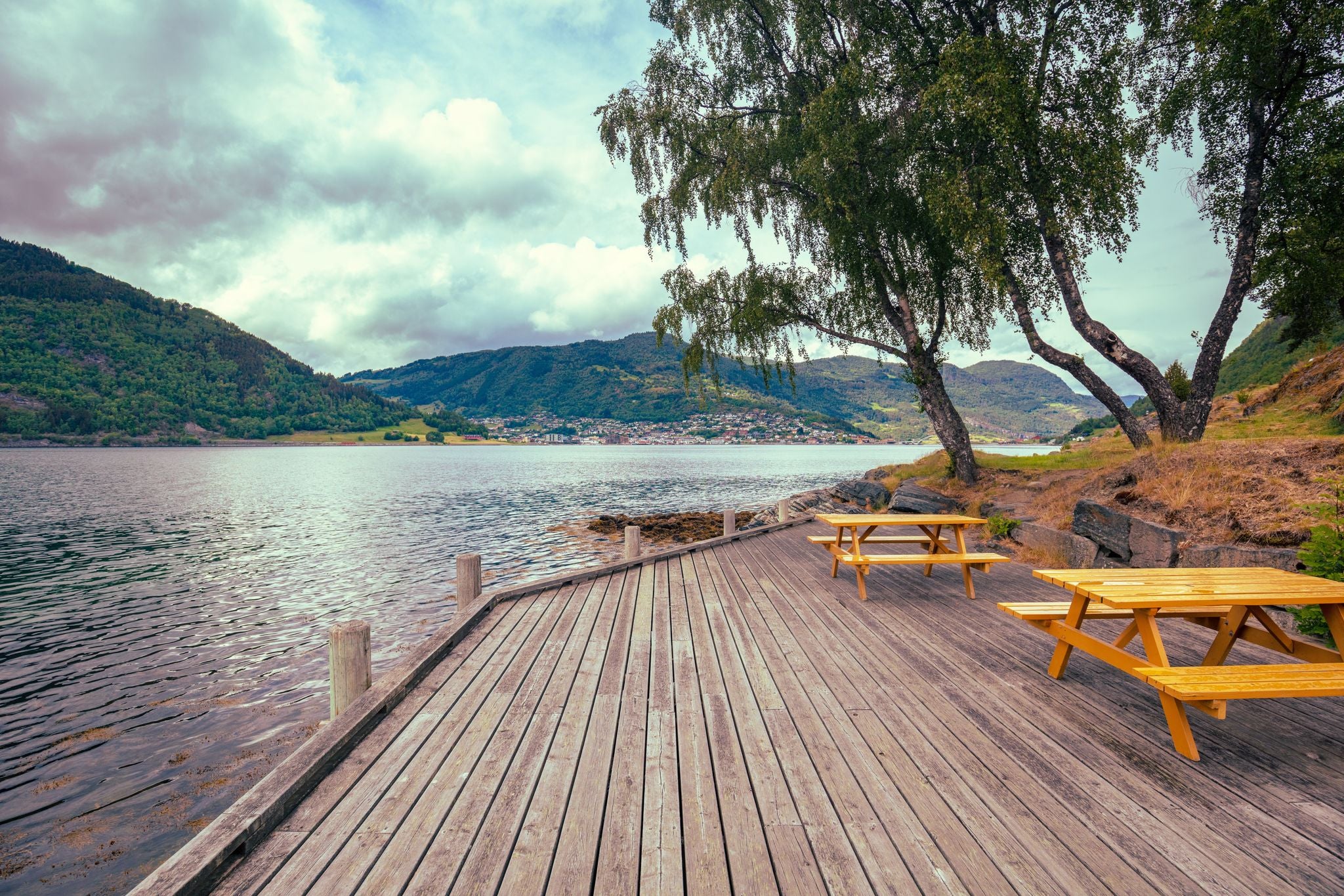 photo of view of View of the Sognefjord on a cloudy day. Wooden embankment with rest place near the fjord. Kjornes Camping, Sogndal, Norway