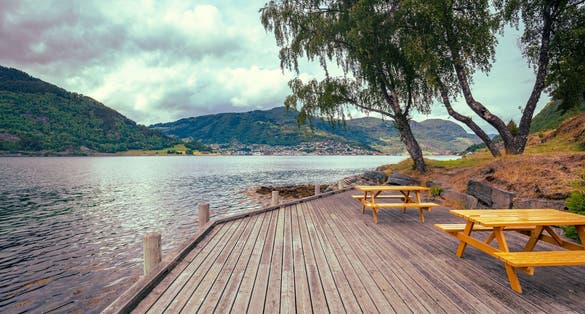 photo of view of View of the Sognefjord on a cloudy day. Wooden embankment with rest place near the fjord. Kjornes Camping, Sogndal, Norway
