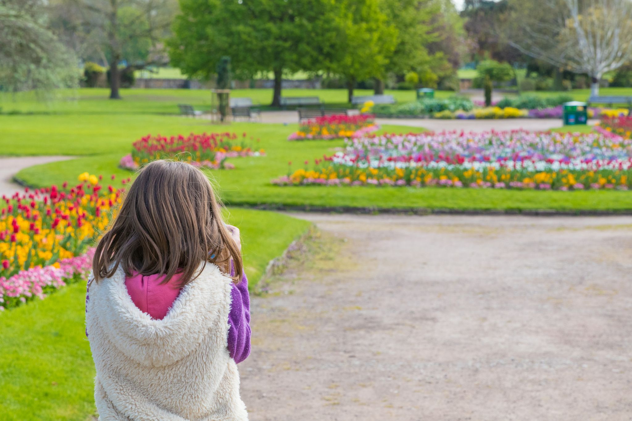 Photo of Young female girl taking photo of the beautiful colourful flower beds and green grass of St Nicholas Park, on a warm spring day, Warwick, United Kingdom.