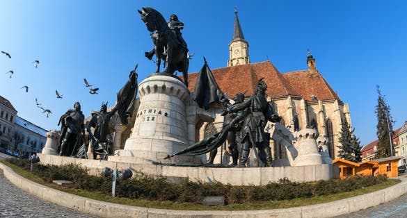 Doves flying over the statue of mathias rex in unirii square, cluj-napoca.