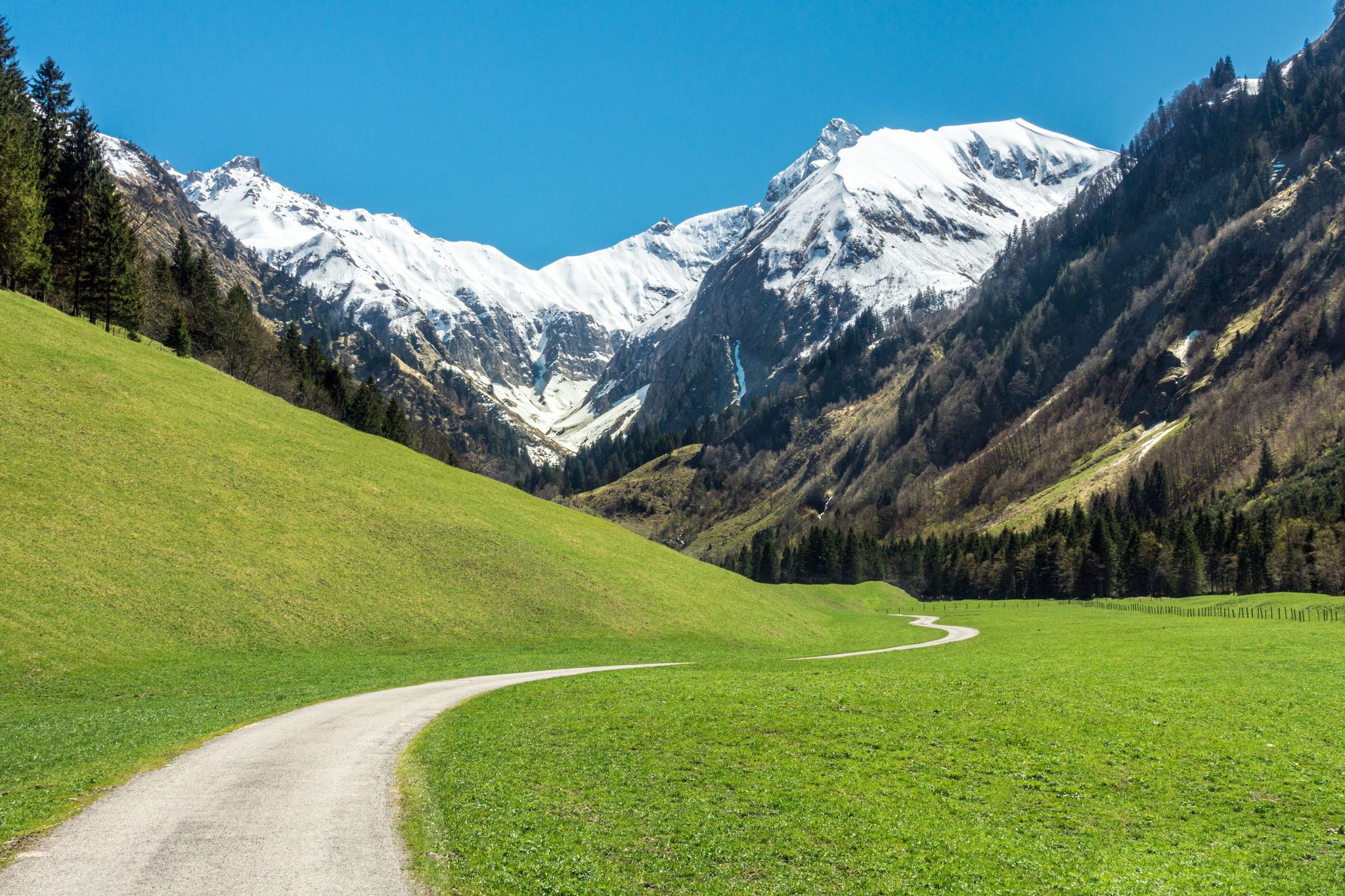 Beautiful landscape with snow capped mountains, green grass meadows and hiking trail in springtime. Trettachtal, Allgaeu, Bavaria, Germany.