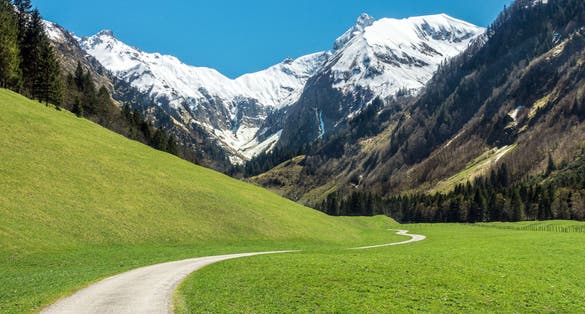 Beautiful landscape with snow capped mountains, green grass meadows and hiking trail in springtime. Trettachtal, Allgaeu, Bavaria, Germany.