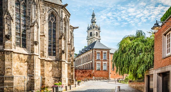 Cobbled street with church and belfry tower in Walloon city center of Mons, Hainaut, Belgium.