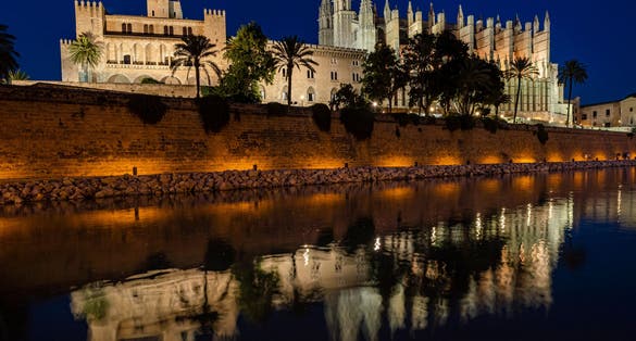photo of night panoramic view of Cathedral of Palma de Majorca and Royal Palace of La Almudaina with a fountain in the fortress in Palma, Spain.