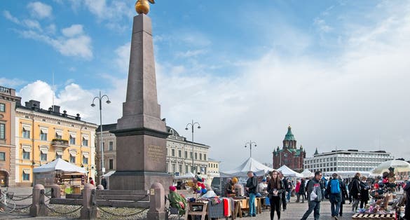 Photo of people on The Market Square near souvenir shops. On the left is The Tsarinas Stone Obelisk. On the background is The Uspenski Cathedral.